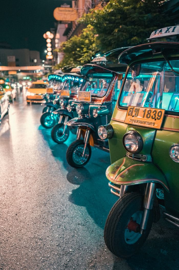 Colorful tuk tuks lined up on a bustling Bangkok street at night with vibrant lights.