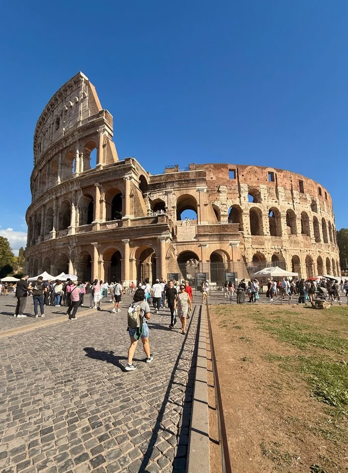 Tourists admire the iconic Colosseum in Rome on a sunny day.