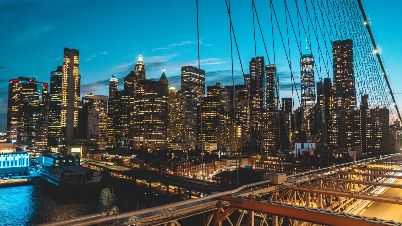 Panoramic view of New York City skyline at twilight from Brooklyn Bridge, showcasing modern skyscrapers.